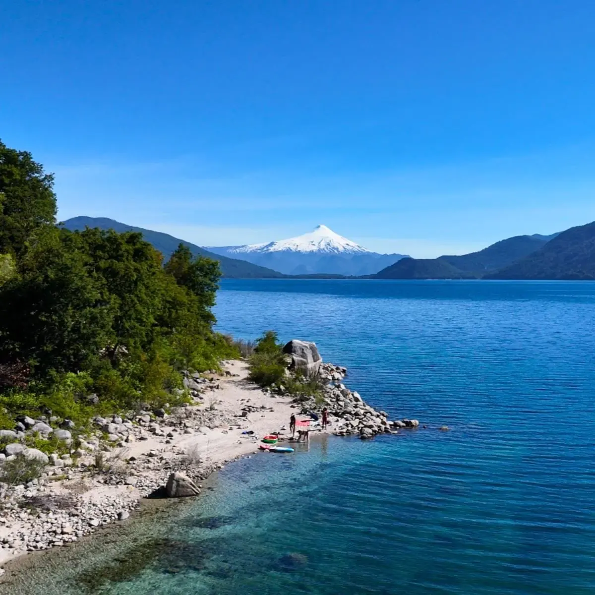 Orilla del lago de aguas cristalinas con el volcán Villarrica nevado al fondo