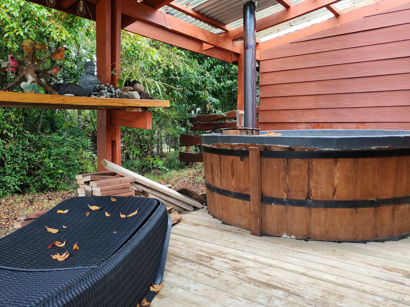 Tinaja de madera con chimenea, en una terraza techada junto a la cabaña