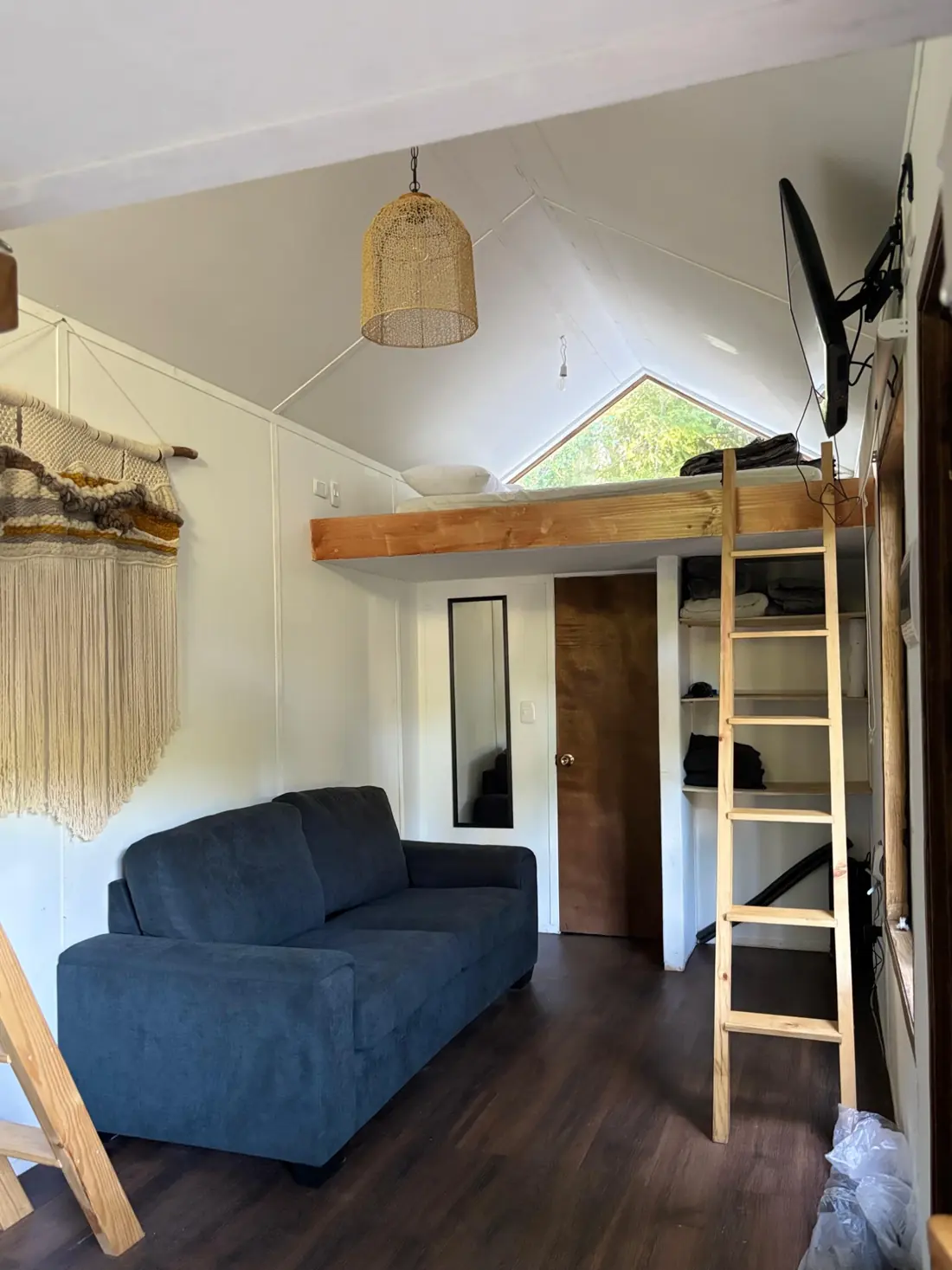 Interior de la tiny house con sofá, escalera y la cama en altillo